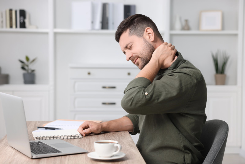 man with neck pain and headache, sitting at desk